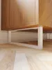 A close-up view of the base of a wooden cabinet with white metal legs, resting on a light wood floor. Náhľad obrázku produktu
