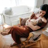 A mother is holding her baby in a rocking chair next to a baby crib. Produktbild-Vorschau