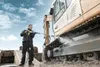 A man is pressure washing the tracks of a large excavator. Produktbild-Vorschau