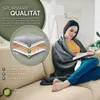 A woman is sitting on a couch, wrapped in a gray blanket, reading a book. Produktbild-Vorschau