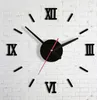 A black wall clock with Roman numerals on a white brick wall. Náhľad obrázku produktu