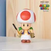 A Toad action figure from The Super Mario Bros. Movie is displayed on a white surface in front of a wooden background. Anteprima dell’immagine prodotto
