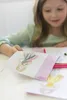A young girl is drawing fashion designs at a table. Anteprima dell’immagine prodotto