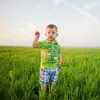 A young boy stands in a grassy field, wearing a green shirt and plaid shorts, with a stethoscope around his neck. Anteprima dell’immagine prodotto