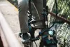 A person riding a black electric bicycle on a path next to a fence. Produktbild-Vorschau