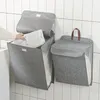 Two grey fabric laundry baskets hanging on a tiled wall. One basket is open and a hand is placing white clothes inside. The other basket is closed. Produktbild-Vorschau