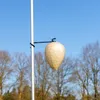 A decorative wasp nest is hanging from a pole against a clear blue sky, with trees in the background. Produktbild-Vorschau