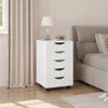 A white rolling storage cart with five drawers is placed next to a bed in a bedroom. Produktbild-Vorschau
