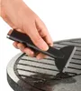 Eine Hand verwendet das Unold Raclette Multi 4 in 1 zum Reinigen der Roste eines runden Grills. Produktbild-Vorschau