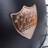 A close-up of a metal badge on a black surface. Náhled obrázku produktu