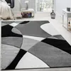A modern geometric rug in black, white, and gray is displayed in a living room setting. Produktbild-Vorschau