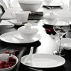 A formal table setting with white porcelain dishes, cutlery, and a wine glass, accented with red berries. Produktbild-Vorschau