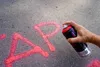 A hand is spraying red chalk on asphalt, forming letters. Produktbild-Vorschau
