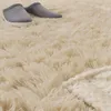 A close-up view of a fluffy cream rug with two gray slippers on it. Produktbild-Vorschau