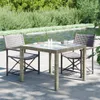 A patio table and chairs set next to a body of water with lush greenery in the background. Produktbild-Vorschau