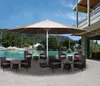 An outdoor patio scene with a large umbrella and seating area overlooking a body of water with boats and a building. Produktbild-Vorschau