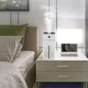 A white humidifier is placed on a nightstand next to a bed, emitting mist. Náhled obrázku produktu