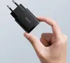 A hand holding a small black USB charger. Produktbild-Vorschau