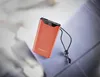 A coral-colored power bank with a black digital display showing '90%' and a black lanyard is placed on a blue surface, with a blurred background of white and light gray fabric. Voir les images du produit