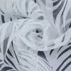 A close-up of white sheer fabric with a leaf pattern, swirled into a rose shape. Produktbild-Vorschau