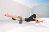 A woman is using a foam roller on her back outdoors. Produktbild-Vorschau