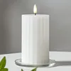 A white LED candle with a ribbed texture sits on a clear glass coaster on a white surface, with a gray background. Podgląd zdjęcia produktu