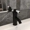 A black faucet with a white handle is shown in a bathroom sink. Náhled obrázku produktu