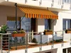 A balcony with a striped awning, railing, and flower boxes. Produktbild-Vorschau