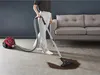 A person is vacuuming a dark spill on a carpeted floor next to a sofa. Voir les images du produit