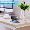 A digital alarm clock and a smartphone are placed on a wooden desk next to a computer monitor and a vase of flowers. Produktbild-Vorschau