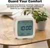 A white digital clock is placed on a wooden table next to a potted plant. The clock displays the time, date, temperature, and humidity. Podgląd zdjęcia produktu