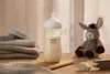A baby bottle filled with milk is placed on a wooden surface next to a stack of towels and a stuffed donkey toy. Podgląd zdjęcia produktu