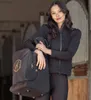 A woman stands in a stable holding a black bag. Produktbild-Vorschau