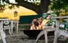 An outdoor seating area with a fire pit, chairs, and a bench under a large tree. Anteprima dell’immagine prodotto