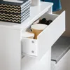 A close-up view of an open drawer in a white cabinet, revealing storage containers and sunglasses. Anteprima dell’immagine prodotto