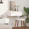 A white dressing table with a drawer and a mirror, placed on a white wall next to a nightstand and a stool. A plant is visible on the right side. Voir les images du produit