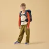A young boy wearing a backpack stands against a plain background. Náhled obrázku produktu