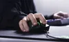 A person's hand is shown using a black gaming mouse on a mousepad, with a keyboard visible in the background. Produktbild-Vorschau