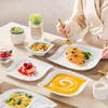 A table setting with various porcelain dishes filled with food, and a person's hands holding a fork over a plate of spaghetti. Náhled obrázku produktu