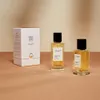 Two bottles of perfume and a box are displayed on a textured surface with a soft, neutral background. Voir les images du produit