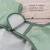Close-up of a green baby bib with white polka dots, showing the velcro closure. Produktbild-Vorschau
