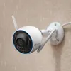 A white security camera mounted on a beige wall during a rain shower. Anteprima dell’immagine prodotto