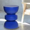 A blue stool is placed on a concrete floor next to a chair. Produktbild-Vorschau