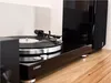 A close-up shot of a turntable with a record playing, placed on a wooden surface next to a speaker. Produktbild-Vorschau