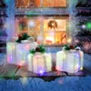 Three illuminated Christmas gift boxes are displayed on a wooden surface covered in snow, with a house window in the background. Anteprima dell’immagine prodotto