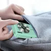 Hands placing a mint green digital camera into a gray fabric bag. Produktbild-Vorschau