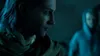 Two people in a dimly lit environment, one in the foreground looking to the side, the other in the background wearing a hoodie. Podgląd zdjęcia produktu