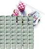 A collection of small glass jars with green and white checkered lids, arranged in stacks, with a decorative background featuring flowers and a recipe booklet. Náhled obrázku produktu