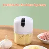 A white electric garlic press filled with chopped garlic sits on a wooden table next to a whole garlic bulb and a bowl of minced meat. Produktbild-Vorschau