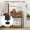 A bedside table with a drawer and shelf, placed next to a bed. A lamp and picture frames are on top of the table. A close-up inset shows the adjustable foot pad of the table's leg. Podgląd zdjęcia produktu